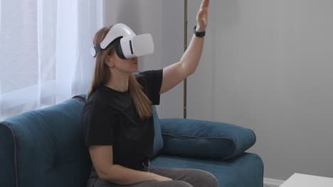 Weibliche-Benutzerin-Verwendet-HMD-Display-Zum-Betrachten-Des-Interieurs-Einer-Modernen-Wohnung,-Sitzt-Auf-Der-Couch-Im-Wohnzimmer-Und-Nutzt-Moderne-Virtual-Reality-Technologie